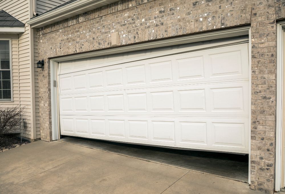 unnamed (13) White sectional garage door closed in a brick house with a concrete driveway.